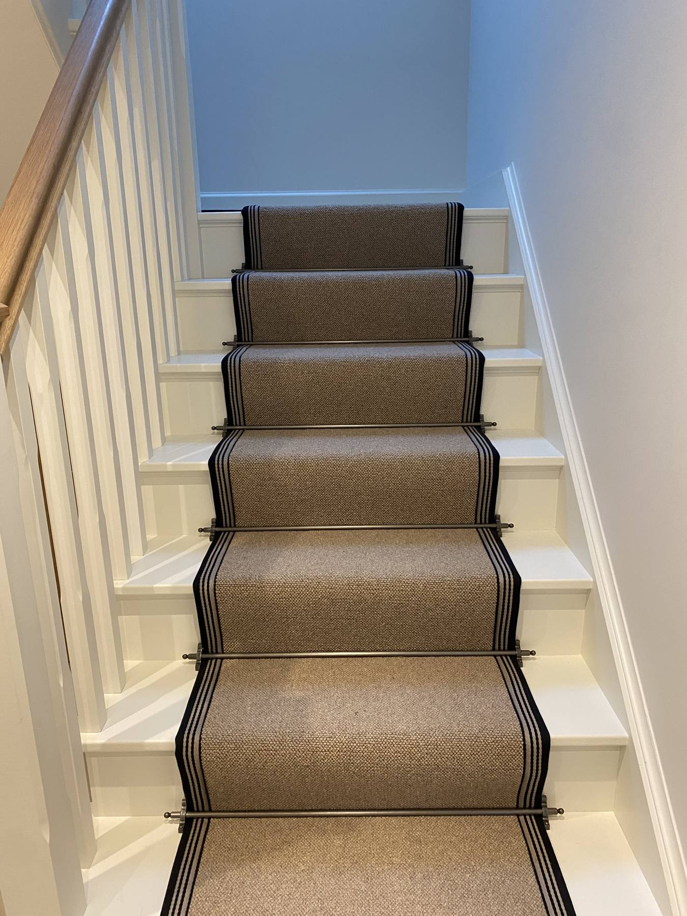 White staircase with a natural weave stair runner, black striped borders and brass stair rods