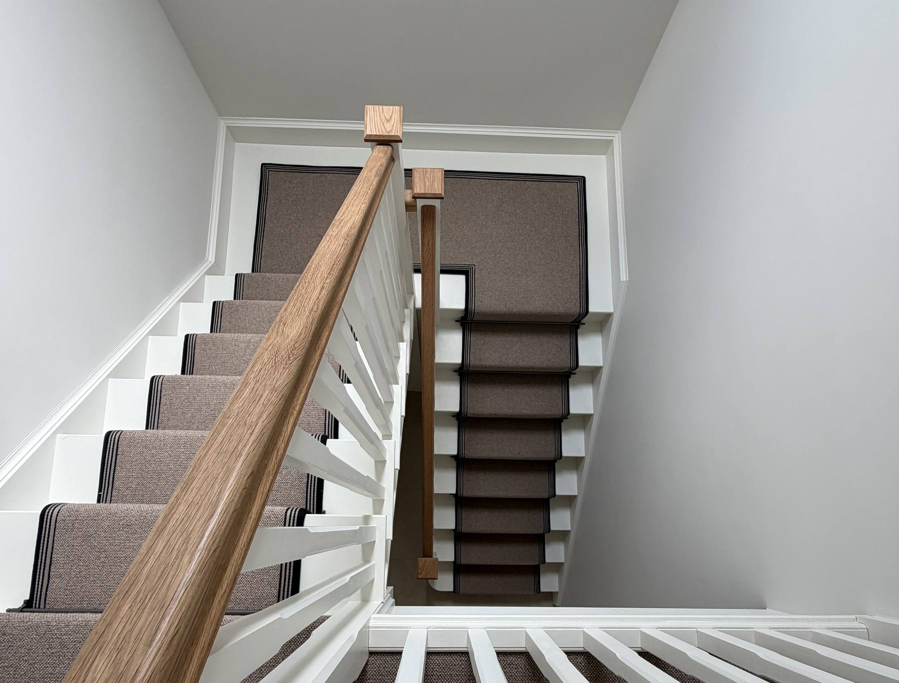 Looking down a white staircase with an oak handrail and a natural weave runner with dark borders